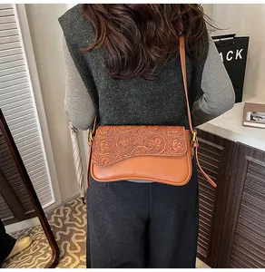 Detailed shot of brown vintage tooling leather shoulder crossbody bag with floral embossed flap.