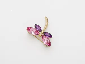 Gros plan détail d'une broche libellule en cristal scintillant avec des strass roses et violets.
