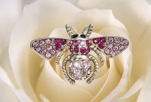 Rhinestone bee brooch detail shot, shiny pink crystals on alloy metal, delicate jewelry.