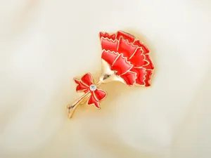 Detailed close-up view of red carnation enamel brooch featuring gold alloy and rhinestone bow.
