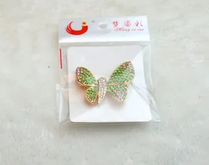 Detailansicht der Strass Schmetterlingsbrosche mit grünen Steinen in transparenter Verpackung.