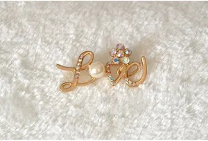 Close-up detail of the gold-tone metal LOVE alphabet brooch featuring sparkling rhinestones.