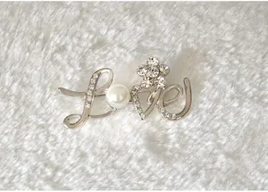 Close-up detail of rhinestone love letter brooch, shimmering crystal and pearl charm decoration.