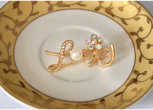 Gold tone LOVE rhinestone letter brooch detail shot, elegant crystal pearl accessory.