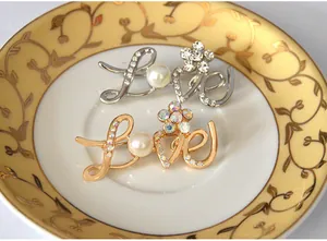 Close-up detail of rhinestone inlaid LOVE letter brooch with pearl accent on decorative plate.