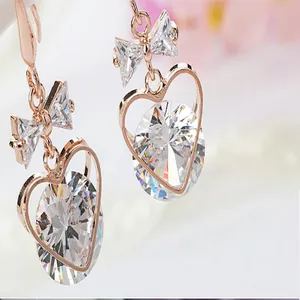 Close-up detail of rose gold heart and bow zircon drop earrings sparkling stones.