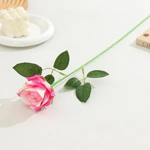 Detailed close-up shot of an artificial pink gradient rose flower with green leaves on desktop.