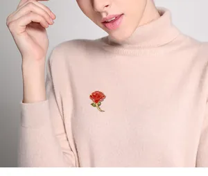 Close-up detail of a red carnation enamel brooch pin worn on a pink turtleneck sweater.