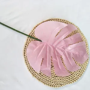 Gros plan d'une feuille de monstera artificielle rose avec tige verte sur tapis tressé.