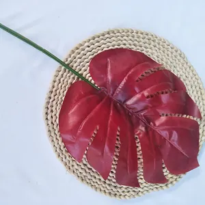 Gros plan sur feuille de monstera artificielle rouge sur tapis tressé pour décoration.