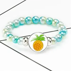Detail view of a beaded pearl bracelet featuring a vibrant yellow pineapple pendant charm