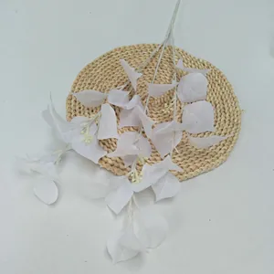 Detail view of white artificial plant leaf branch on woven mat, ideal for home decor floral design.