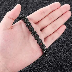 Close-up detail of a men's black stainless steel Byzantine chain bracelet held in a hand