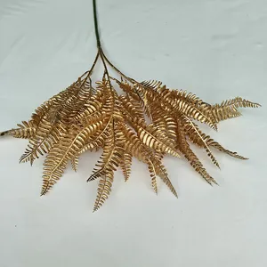 Gold artificial fern plant detail view, shiny metallic branch for wedding floral decor.