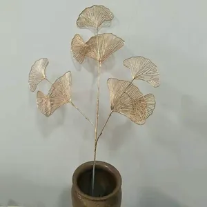 Detail view of golden metal ginkgo leaf branch simulation plant decor in ceramic vase.