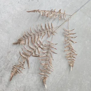 Close-up of golden artificial fern leaf branch, metallic texture for wedding decor display.