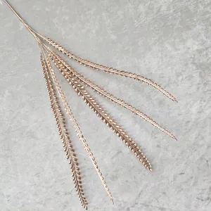 Detailed close-up shot of an elegant gold artificial fern branch, perfect for wedding decor.