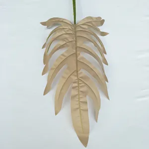 Golden artificial monstera leaf detail close up, textured fake plant branch for wedding decor.