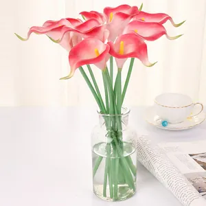 Gros plan de lys arums artificiels roses en vase en verre avec accessoires pour vue de détail.