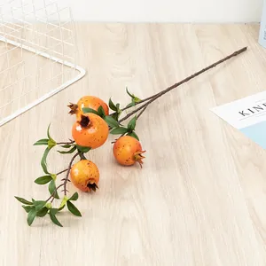Artificial pomegranate branch detail showing realistic orange fruit and green leaves.