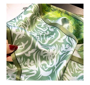 Green silk scarf detail shot showing luxurious smooth fabric texture and artistic pattern design.