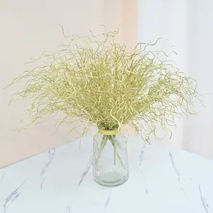 Golden curly decorative branches displayed in a clear glass vase on a marble table.