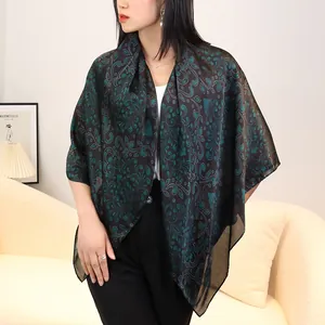 Detail view of a black and green silk-feel scarf worn by a model in a cozy room setting.