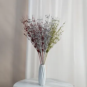 Vista dettagliata di rami di bacche scintillanti di Natale in un vaso geometrico bianco.