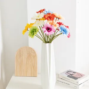 Primo piano dettagliato di fiori di gerbera artificiali colorati in un vaso bianco moderno sul tavolo.