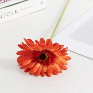 Primo piano dettagliato di un fiore di gerbera artificiale arancione con stelo verde per arredo interno.