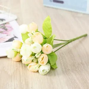 Close-up detail of artificial mini rose bouquet, cream yellow flower buds with green leaves.