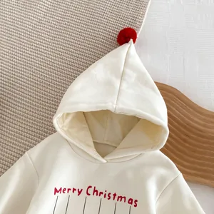 Détail de combinaison bébé polaire Noël à capuche, vêtement blanc avec pompon rouge.
