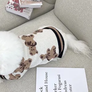 Jersey blanco de punto con ositos marrones y borde a rayas, puesto en un perro sobre sofá gris