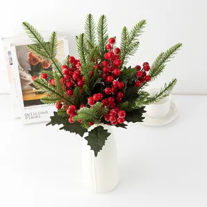 Branches de pin artificiel de Noël baies rouges et feuilles givrées dans vase blanc.