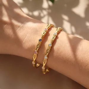 Detailansicht vergoldeter Edelstahl-Armreifen mit bunten Zirkoniasteinen am Handgelenk.