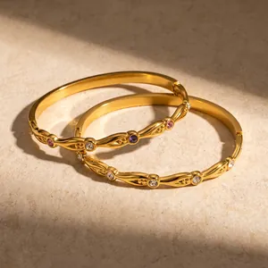 Detailaufnahme von 18k vergoldeten Armreifen mit Wellenmuster und bunten Zirkoniasteinen.