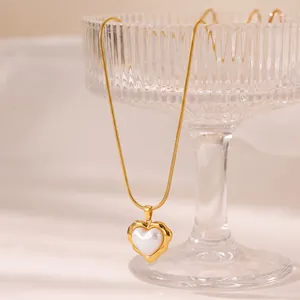 Detalle de un collar con colgante de corazón dorado e incrustación de perla en cadena de serpiente.