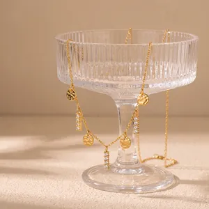 Nahaufnahme einer goldenen Edelstahlkette mit Hammerschlag-Anhängern und Strass auf einem Glas.