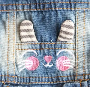 Close-up of cute pink bunny face embroidery and striped ears on pet denim vest.