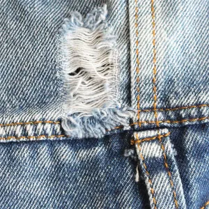 Primo piano del tessuto denim strappato con cuciture arancioni su un gilet per animali.