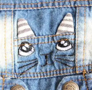 Detailed view of the cat face embroidery on a blue denim vest for small pets