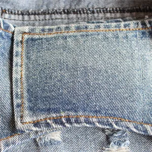 Vista macro del tessuto denim blu invecchiato di alta qualità con dettagli di cuciture arancioni