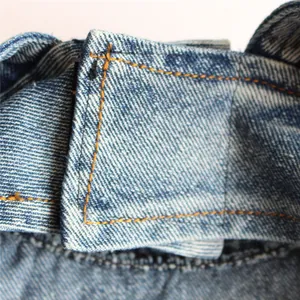 Dettaglio ravvicinato di resistente tessuto denim blu e cuciture gialle rinforzate.