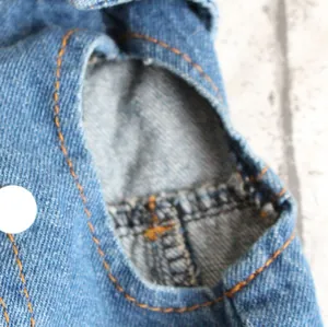 Close-up detail shot of a pet denim vest armhole featuring orange stitching and a white button
