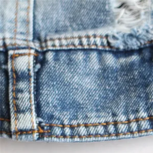 Inquadratura macro ravvicinata del denim azzurro con cuciture arancioni e bordo sfrangiato