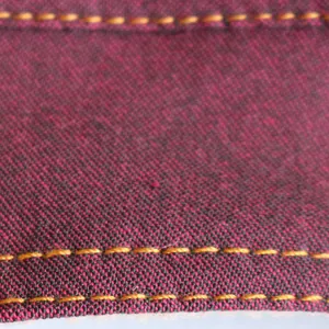 Makroaufnahme einer Hunde-Jeansweste mit kastanienbrauner Textur und gelber Naht.