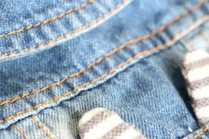 Detailed macro shot of durable blue denim fabric with orange stitching on a pet vest