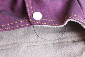 Detail einer Denim-Haustierweste mit Fleece-Futter und weißem Druckknopfverschluss.