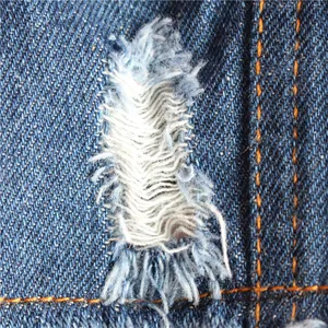 Makro-Detail von distressed blauem Denim-Stoff mit Fransen an einer Haustierweste.