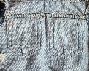 Detailed view of blue denim pet vest featuring distressed pockets and yellow stitching